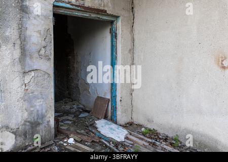 Weathered doorway in a decaying concrete structure with peeling paint, exposed brick, and debris-covered floor suggesting neglect and abandonment. Stock Photo