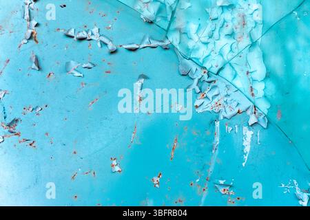 Close-up of cracked and peeling turquoise paint on a rusted metal surface, showing texture and decay in vibrant color contrast. Stock Photo