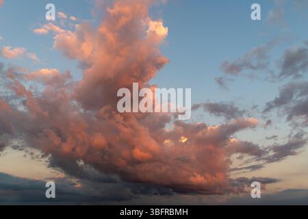 Large cumulus clouds illuminated with intense warm orange and red sunset light against a fading blue sky. Stock Photo
