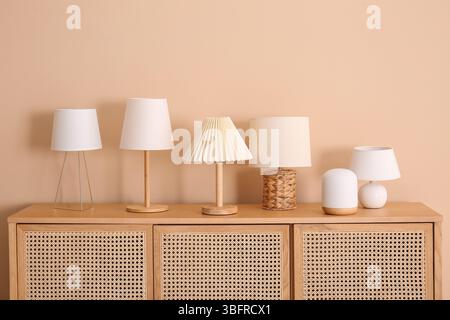 Set of different table lamps on wooden cabinet near beige wall Stock Photo