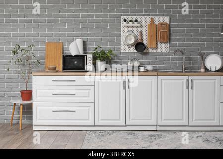 Interior of modern kitchen with white counters and pegboard hanging on grey brick wall Stock Photo