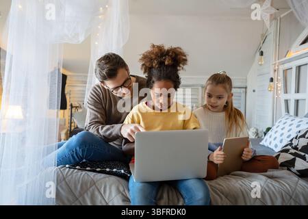 Excited single father plays with diverse, multi-ethnic daughters. Using digital tablet enjoy weekend Stock Photo