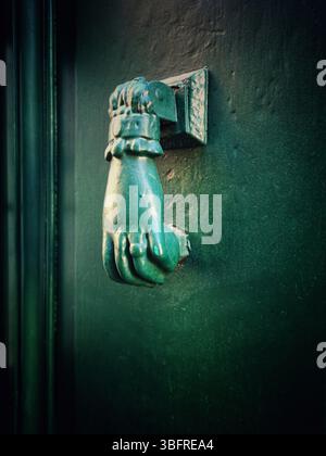A distinctive bronze hand-shaped door knocker is mounted on a teal door Stock Photo