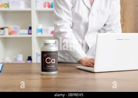 Female pharmacist working with laptop and pill bottle on table at pharmacy, closeup Stock Photo