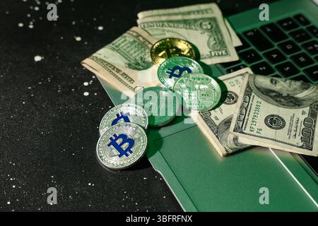 Laptop with bitcoins and dollar banknotes on black table, closeup Stock Photo