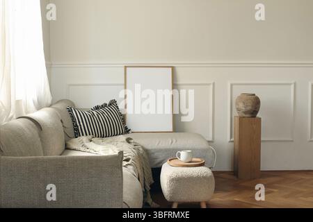 Empty wooden picture frame on grey sofa, striped pillow. White stucco panelled wall. Minimal elegant poster mockup. Artistic template. Cup of coffee Stock Photo
