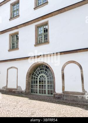 Historic building facade featuring distinctive arched and rectangular windows with stone trim. The cobblestone path in front adds charm, highlighting Stock Photo