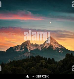 A majestic mountain formation, the Watzmann in Bavaria, Germany, with a colorful sunset sky and dark woodlands in the foreground Stock Photo