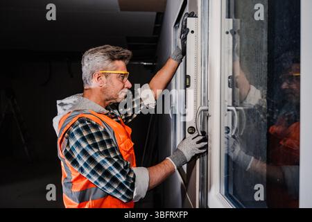 A window installer checks the vertical alignment of a sliding glass door frame using a spirit level. Indoor renovation work with precision tools Stock Photo