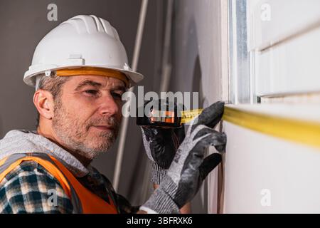 Focused construction worker using a tape measure to ensure accurate dimensions during wall installation at the building site Stock Photo
