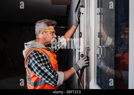A window installer checks the vertical alignment of a sliding glass door frame using a spirit level. Indoor renovation work with precision tools and s Stock Photo