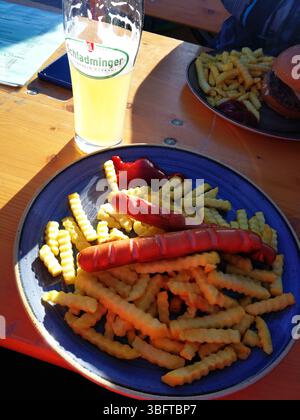 Plate of Fries and Sausages with Beverage on Patio Table. Schladming, Austria Stock Photo
