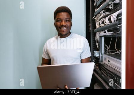 Young technician working in server room, managing cables and technology efficiently while smiling Stock Photo