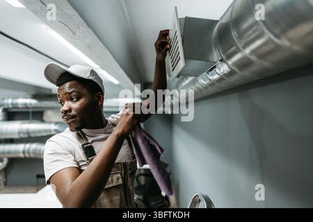 Worker performs maintenance on ventilation system in commercial building during daytime hours Stock Photo