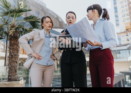 Three businesswomen collaborating and reviewing documents outdoors, showcasing teamwork Stock Photo