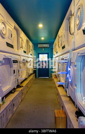 Bali, Indonesia - Dec 10, 2024: Row of white bunk beds with blue doors and a blue ceiling. The beds are in a hallway with a blue door Stock Photo