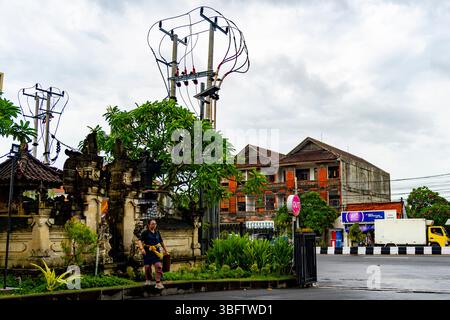 Bali, Indonesia - Dec 10, 2024: Woman is walking in front of a temple. The sky is cloudy and the street is empty Stock Photo