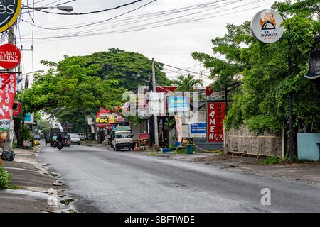 Bali, Indonesia - Dec 10, 2024: Street with a lot of trees and a sign for a ramen restaurant. The street is busy with cars and motorcycles Stock Photo