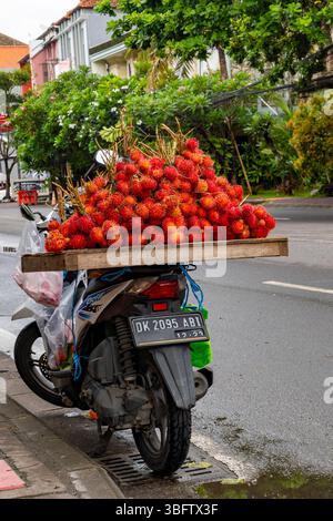 Bali, Indonesia - Dec 10, 2024: Man is selling fruit called rambutan on a motorcycle. The fruit is red and there are many of them Stock Photo