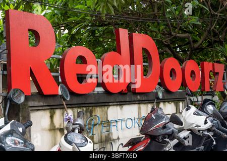 Bali, Indonesia - Dec 10, 2024: Red sign with the word Reddoorz written on it. The sign is surrounded by parked motorcycles Stock Photo
