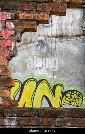 Bali, Indonesia - Dec 10, 2024: Wall with graffiti on it and a hole in it. The graffiti is mostly yellow and blue Stock Photo