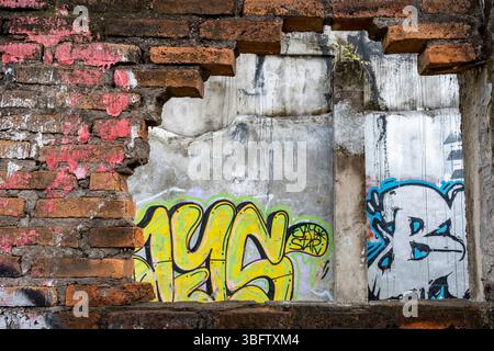 Bali, Indonesia - Dec 10, 2024: Wall with graffiti on it and a hole in it. The graffiti is mostly yellow and blue Stock Photo