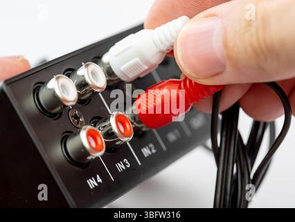 Closeup of a hand plugging in red and white RCA cables into the audio input ports on modern device, macro closeup detail view, analog connection sound Stock Photo