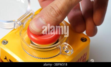 Closeup of a finger hand pressing a red nuclear weapon missile launch button on a yellow weapon control console, symbol of atomic warfare, doomsday sc Stock Photo