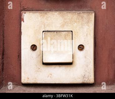 Old dirty electric light switch or doorbell button on a rusty red wall surface, vintage damaged electric button, worn out plastic, retro building indo Stock Photo