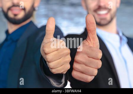 Two confident businessmen in suits giving thumbs up and smiling at camera Stock Photo