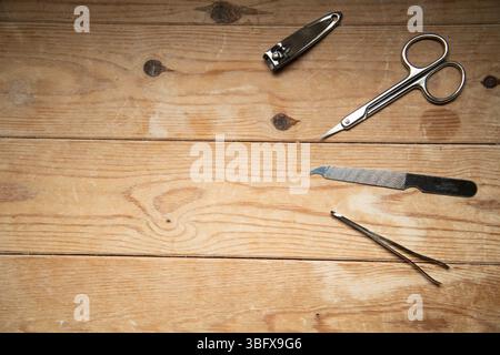Nail grooming tools—file, scissors, clippers, tweezers—neatly arranged on a wooden slatted background, top-down view. Stock Photo