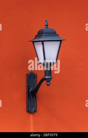 A black metal lantern fixed on a red wall, captured in daylight. The image highlights the contrast between the classic lantern design and the vivid or Stock Photo