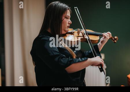 Young woman playing a violin passionately in indoor ambient lighting Stock Photo
