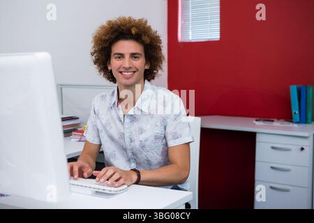 Man typing on keyboard at small office desk with desktop monitor, notebooks, papers and binders Stock Photo