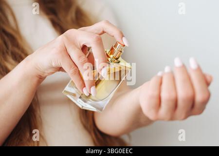 Woman spraying perfume. Holding golden glass bottle. Elegant gesture on wrist. Fragrance application closeup. Stylish beauty product in female hand. Stock Photo