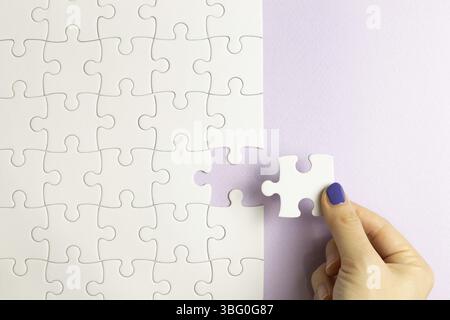 Set of white puzzle pieces and hand holding last one piece on purple background. top view Stock Photo