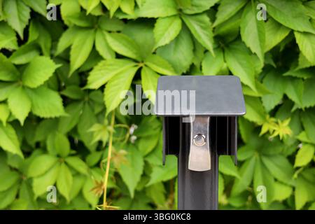 Shiny, silver gate opening button on the metal post with a lush green plants background Stock Photo