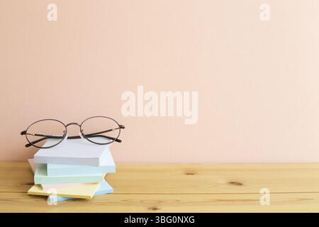 Glasses and stack of colorful memo pad, sticky notes on wooden desk. Pink background, copy space. Work and study place Stock Photo