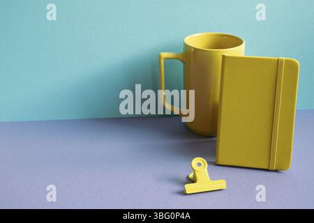 Yellow notebook and mug cup, clip on purple desk. blue background Stock Photo