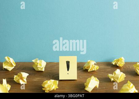Crumpled paper balls and notepad with exclamation mark on wooden desk. blue wall background. Thinking, solution, business, idea concept Stock Photo