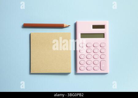 Pink digital calculator and memo note pad and brown colored pencil on blue background Stock Photo
