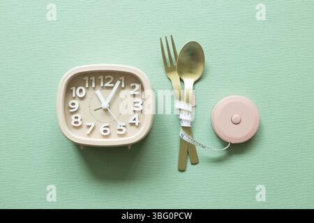 Fork and spoon with measuring tape, clock on green background. Diet concept Stock Photo