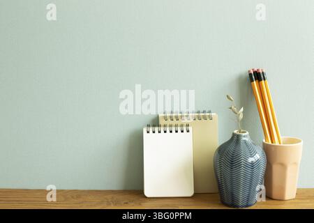 Notebook, pencil, eucalyptus on wooden desk. blue wall background. workspace Stock Photo