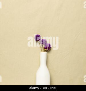 Vase of purple globe amaranth flowers on beige fabric background. flat lay, top view, copy space Stock Photo