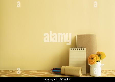 Notebook, colored pencils, flower on wooden desk. beige background. Work and study place Stock Photo