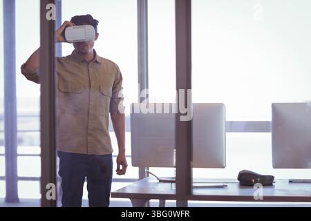 Man wearing VR headset interacting near glass partition in modern office with dual monitors Stock Photo