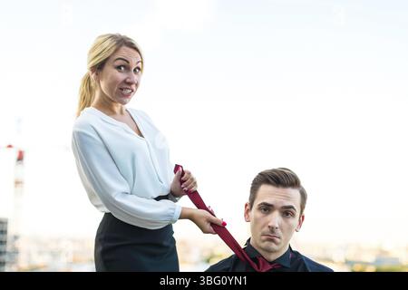Couple of caucasian businessmen, young attractive brunette man in dark suit, red tie and black shirt, and pretty blonde woman in white blouse and blac Stock Photo
