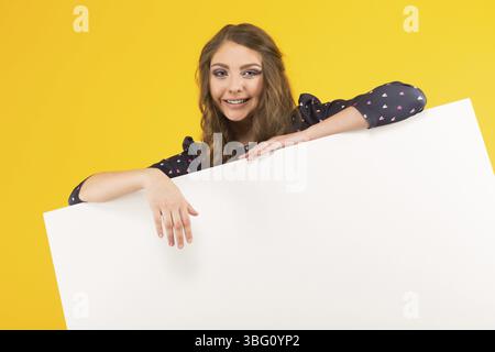 Portrait of attractive happy brunette woman in blouse isolated on yellow background holding emty blank board your text here concept Stock Photo