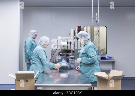 Pharmaceutical technicians work in sterile working conditions at pharmaceutical factory. Scientists wearing protective clothing Stock Photo