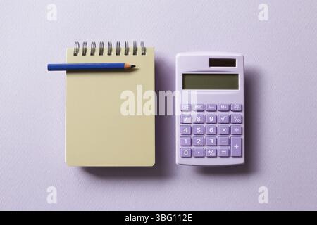 Beige notepad and calculator isolated on purple background. top view, copy space Stock Photo